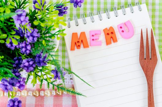 Open diary and wooden spoon fork with flower on beautiful fabric background. Menu concept.