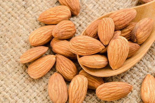 Almonds in wooden spoon on sack background.
