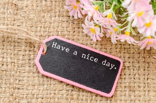 Have a nice day on wooden tag and copy space for your text with flower on sack background.
