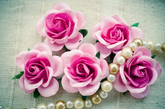 Vintage pink rose and pearl necklace on fabric background.