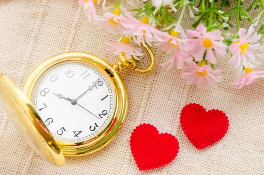 Gold pocket watch and red heart with flower on sack background. Love concept.