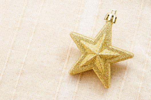 Gold five pointed star christmas decoration on fabric background.