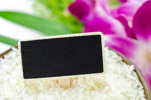 Raw rice and blank black wooden tag for your text with violet orchid on white background.
