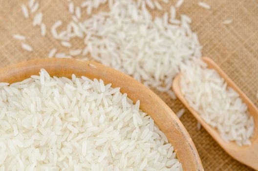 Raw rice in wooden bowl on sack background.