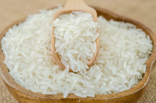 Raw rice and wooden spoon in wooden bowl on sack background.
