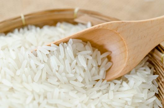 Raw white rice and wooden spoon in weave basket on sack background.