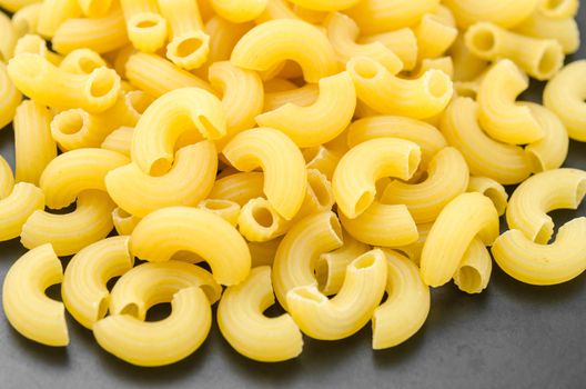 Elbow macaroni noodles on black dish background.