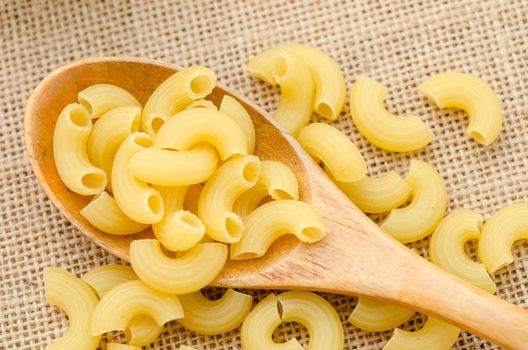 Italian Raw Macaroni Pasta in wooden spoon on sack background.