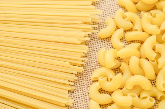 Raw Spaghetti and elbow macaroni. Italian Pasta raw food collection on sack background.