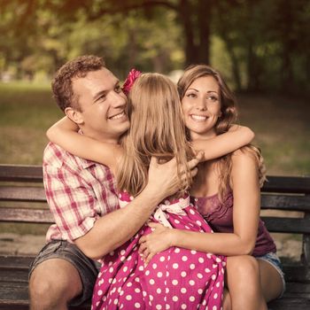 Beautiful little girl embraced her parents in the park.