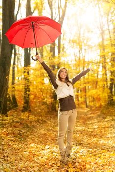 Beautiful cheerful young woman with red umbrella having fun in sunny forest in autumn colors.