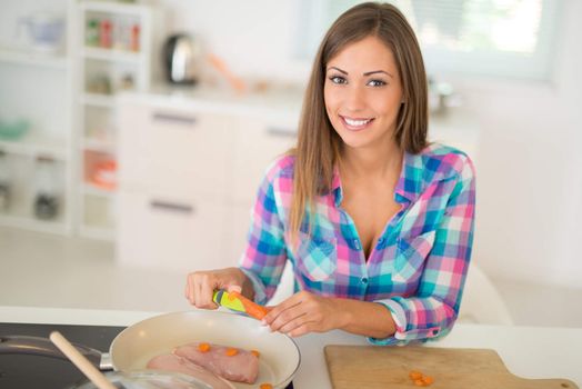 Beautiful young woman cuting carrot and preparing healthy meal in the domestic kitchen. 