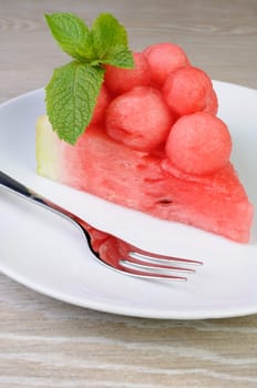 piece of watermelon with watermelon balls and mint on a plate