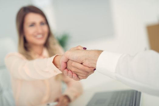 Business woman with face out of focus shakes hands with business man who can see only the hand.