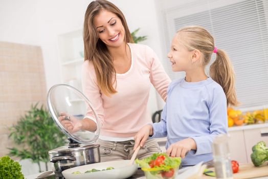 Young beautiful mother and her cute daughter cooking healthy meal in the kitchen.