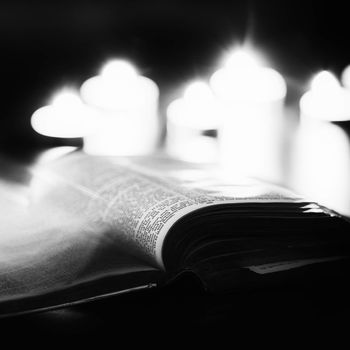 Bible with candles in the background. Low light high contrast black and white image.