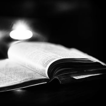 Bible with candles in the background. Low light high contrast black and white image.