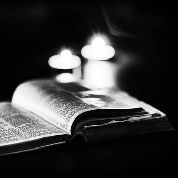 Bible with candles in the background. Low light high contrast black and white image.