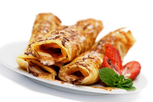 Pancake Tubules with Strawberry, Chocolate Glaze and Mint Leafs on Plate closeup on White background. Focus on Foreground