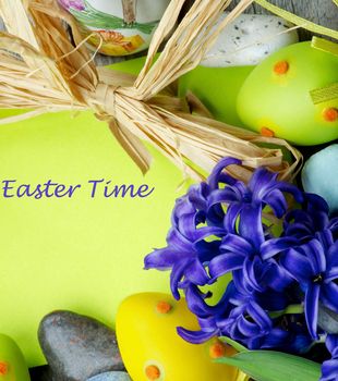 Easter Greeting Card with Crocus, Colored Stones, Easter Eggs and Dry Grass with Empty Green Place to Congratulations and Inscription