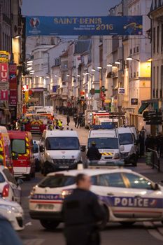 FRANCE, Saint-Denis: Policemen and Paramedics stand at the entrance of a security perimeter set in the northern Paris suburb of Saint-Denis city center, on November 18, 2015, to secure the area after French Police special forces raid an appartment, hunting those behind the attacks that claimed 129 lives in the French capital five days ago. At least one person was killed in an apartment targeted in the operation aimed at the suspected mastermind of the attacks, Belgian Abdelhamid Abaaoud, and police had been wounded in the shootout.