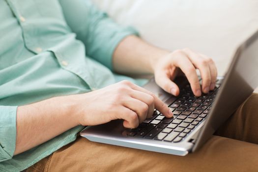 technology, home and lifestyle concept - close up of man working with laptop computer and sitting on sofa at home