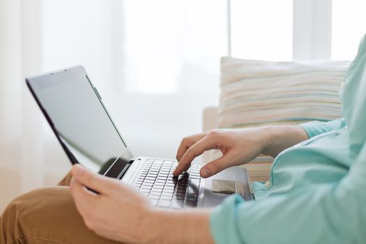 technology, home and lifestyle concept - close up of man working with laptop computer and sitting on sofa at home