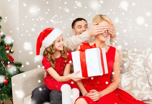 christmas, holidays, happiness and people concept - smiling family in santa helper hats with gift box at home