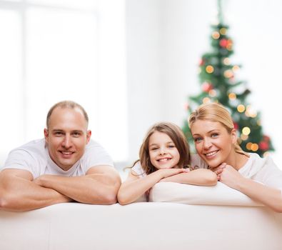 family, childhood, holidays and people - smiling mother, father and little girl over living room and christmas tree background