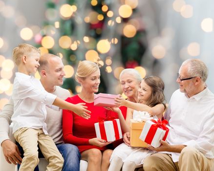 family, holidays, generation, christmas and people concept - smiling family with gift boxes sitting on couch over tree lights background