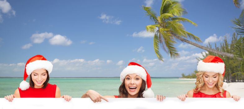 christmas, x-mas, people, advertisement and sale concept - happy women in santa helper hat with blank white board over tropical beach background