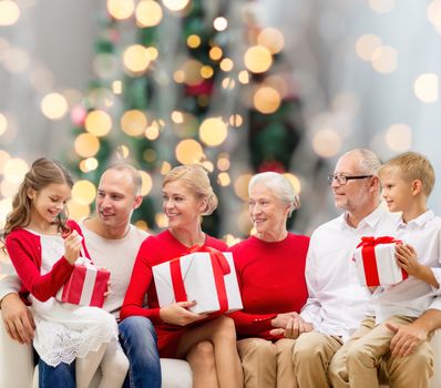 family, holidays, generation, christmas and people concept - smiling family with gift boxes sitting on couch over tree lights background