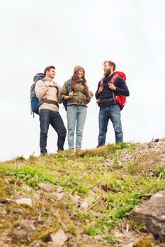 adventure, travel, tourism, hike and people concept - group of smiling friends with backpacks standing on hill and talking outdoors