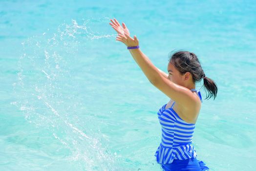 Girl in a blue swimsuit playing splashing water at the sea near beach with happiness during summer at Koh Miang Island, Mu Ko Similan National Park, Phang Nga province, Thailand