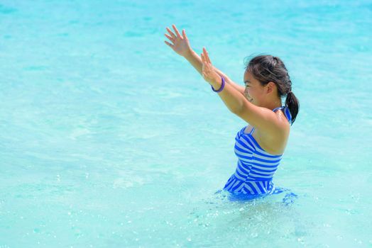 Girl in a blue swimsuit playing splashing water at the sea near beach with happiness during summer at Koh Miang Island, Mu Ko Similan National Park, Phang Nga province, Thailand