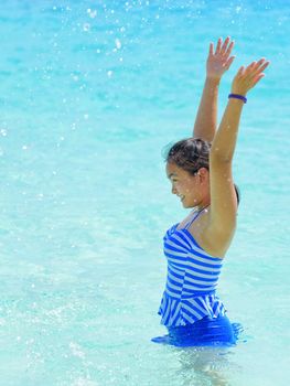 Girl in a blue swimsuit playing splashing water at the sea near beach with happiness during summer at Koh Miang Island, Mu Ko Similan National Park, Phang Nga province, Thailand