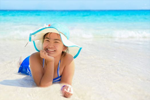 Girl in swimsuit wearing a blue hat lying in the sea with a happy face on the beach during summer at Koh Miang Island, Mu Ko Similan National Park, Phang Nga province, Thailand