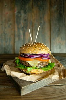 Gourmet burger with melted cheese, tomato and onion filling on top of a wooden chopping board