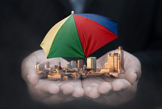 Business man holding company buildings with umbrella protection