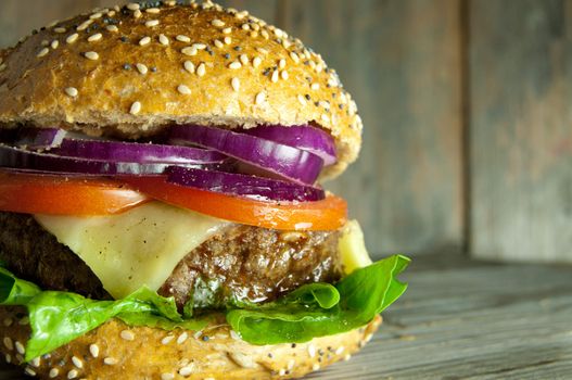 Gourmet burger with cheese, tomato and onion filling on top of a wooden chopping board