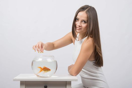 A young girl sits next to a round aquarium in which swimming goldfish
