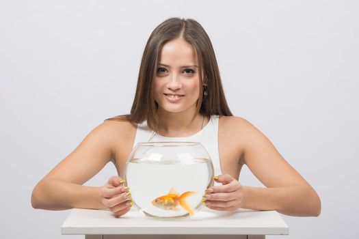 A young girl sits next to a round aquarium in which swimming goldfish