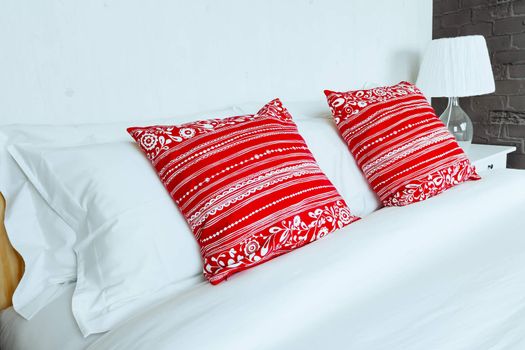 Red pillow on bedroom with white bed sheet and lamp