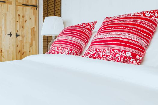 Red pillow on bedroom with white bed sheet and lamp