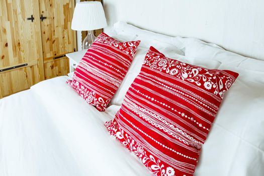 Red pillow on bedroom with white bed sheet and lamp