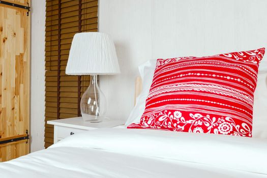 Red pillow on bedroom with white bed sheet and lamp