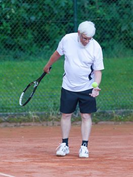 Senior man playing tennis on a gravel court