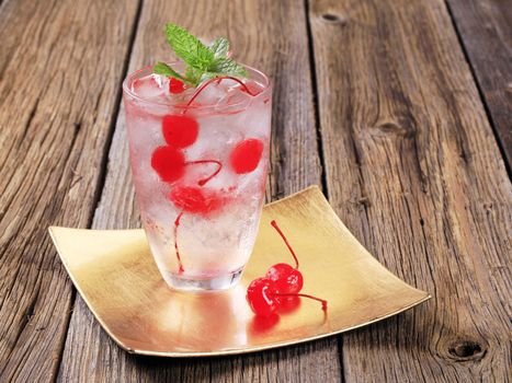 Glass of iced drink with maraschino cherries