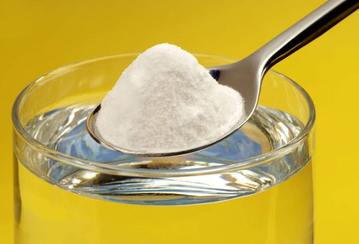 Spoon of baking soda above a glass of water