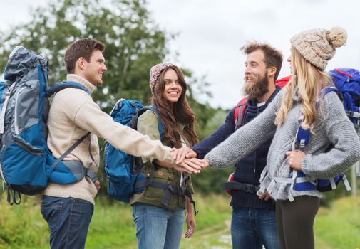 travel, tourism, hike, gesture and people concept - group of smiling friends with backpacks putting hands on top of each other